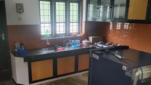 Une cuisine équipée d’un évier, d’une cuisinière et de placards. On y trouve une fenêtre avec des stores, un réfrigérateur et un pare-feu en carreaux.