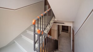 A staircase with metal railings and orange safety tape, leading to a landing with a door and a hallway. - Brand New 2026 apartment + Free On-site Parking (Riga)