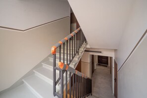 Eine Treppe mit Metallgeländern und orangefarbenem Absperrband, die zu einem Zwischenpodest mit einer Tür und einem Flur führt.