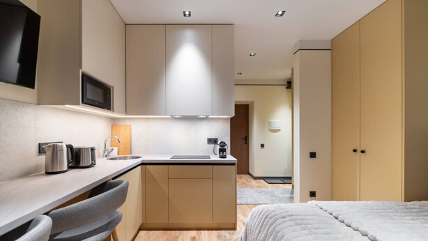 A compact kitchen with a microwave, kettle, and coffee maker, a small dining area with chairs, and a bed with a white duvet. - Brand New 2026 apartment + Free On-site Parking (Riga)