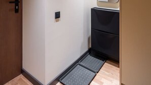 A modern bathroom with a wooden door, a mirror, a light switch, and a small shelf. - Brand New 2026 apartment + Free On-site Parking (Riga)