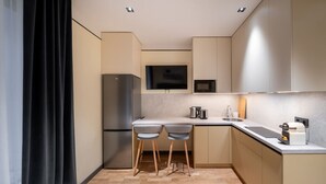 A compact kitchen with a refrigerator, microwave, and a small bar area with stools. - Brand New 2026 apartment + Free On-site Parking (Riga)