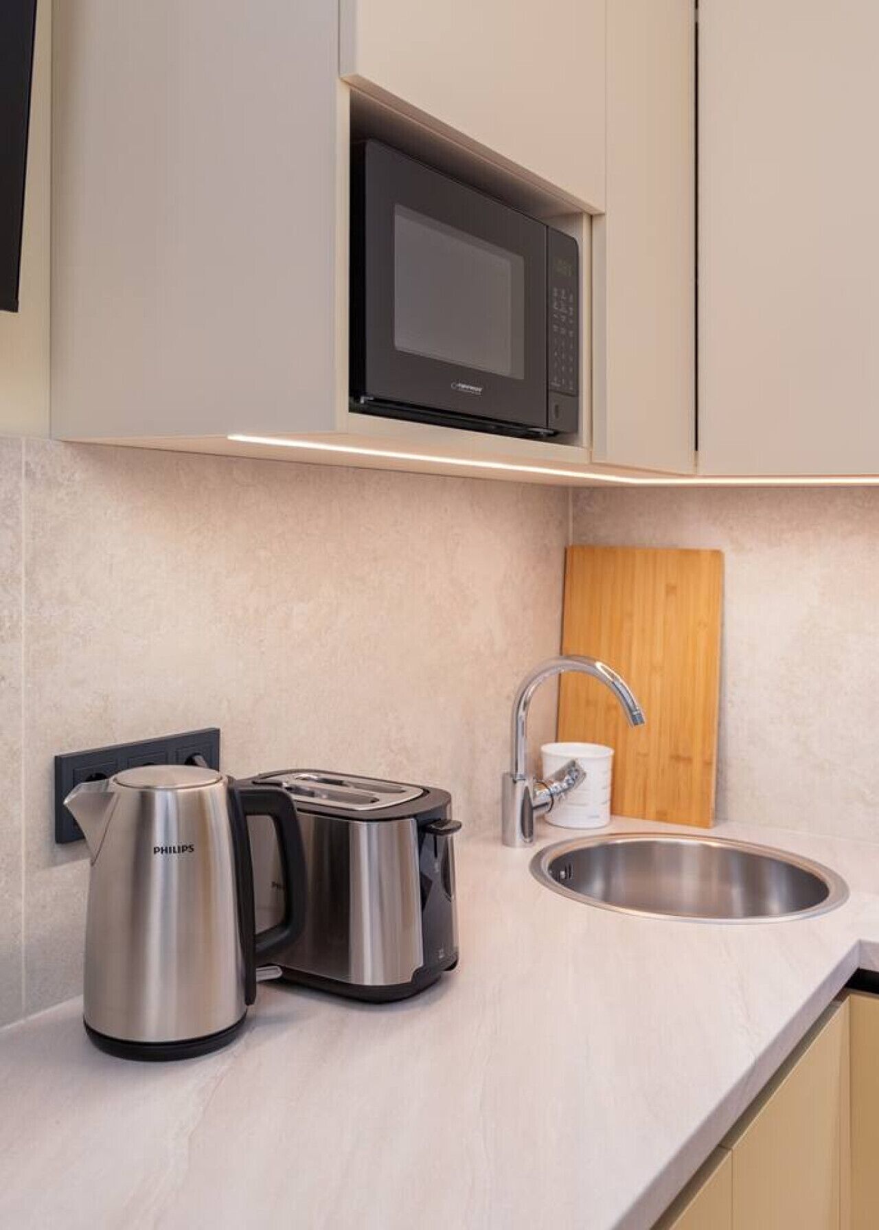 Een moderne keuken met een ingebouwde magnetron, waterkoker, broodrooster en spoelbak.