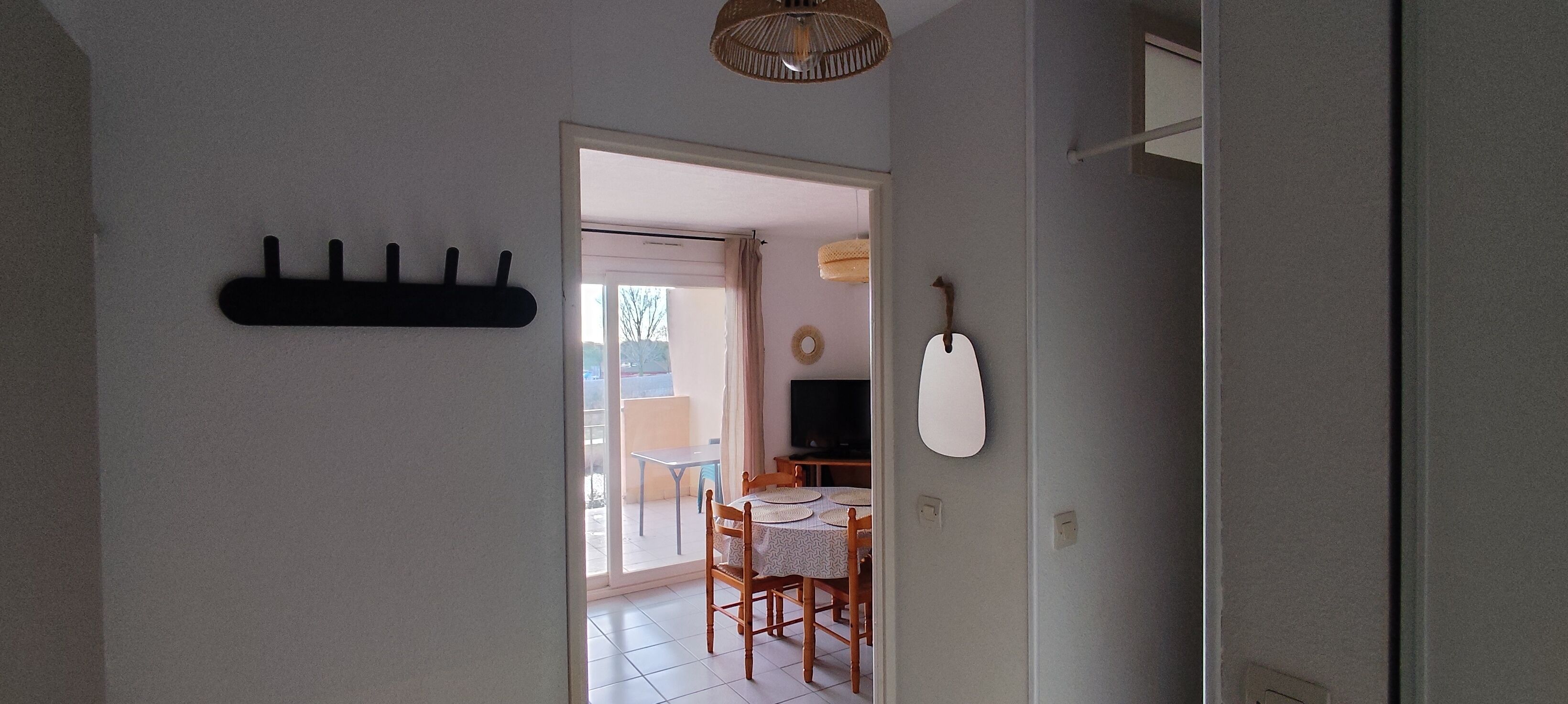 Un pasillo con un perchero, un espejo en la pared y una puerta que da a un comedor con mesa y sillas.