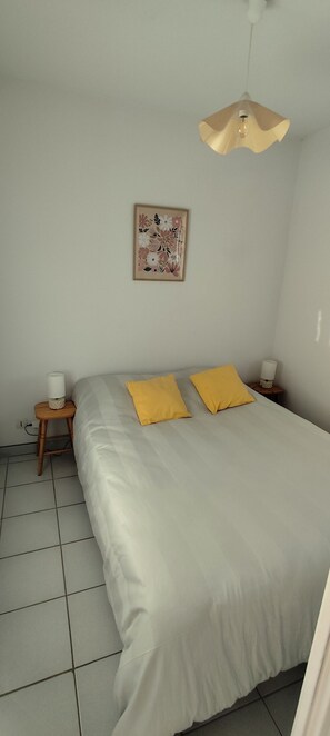 Une chambre à coucher comprenant un lit, deux tables de chevet, un luminaire fixé au mur et une œuvre d’art à motifs floraux.