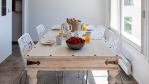 A dining area with a wooden table, white chairs, a bowl of fruit, and a basket of bread. - Villa With Swimming Pool, Sauna, Fitness, sea View (Biot)