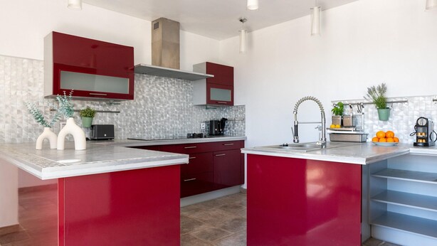 A modern kitchen with red cabinetry, a central island, and a tiled backsplash. - Villa With Swimming Pool, Sauna, Fitness, sea View (Biot)
