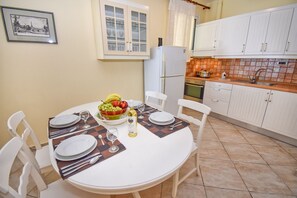 A dining table set with plates, cutlery, and a bowl of fruit and wine. - Tyche Two Bedroom Apartment (Pelekas)