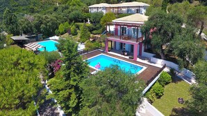 Ein zweistöckiges Haus mit Swimmingpool, umgeben von üppiger Vegetation und Hügeln.