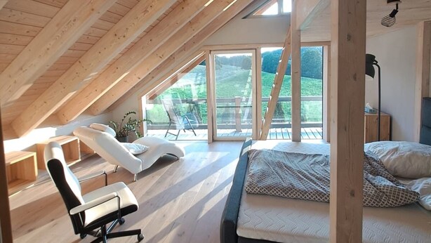 Une chambre spacieuse située dans les combles, avec un plafond en pente, un lit, un bureau et une chaise.