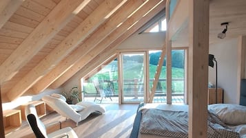 A spacious attic bedroom with a sloped ceiling, a bed, a desk, and a chair.