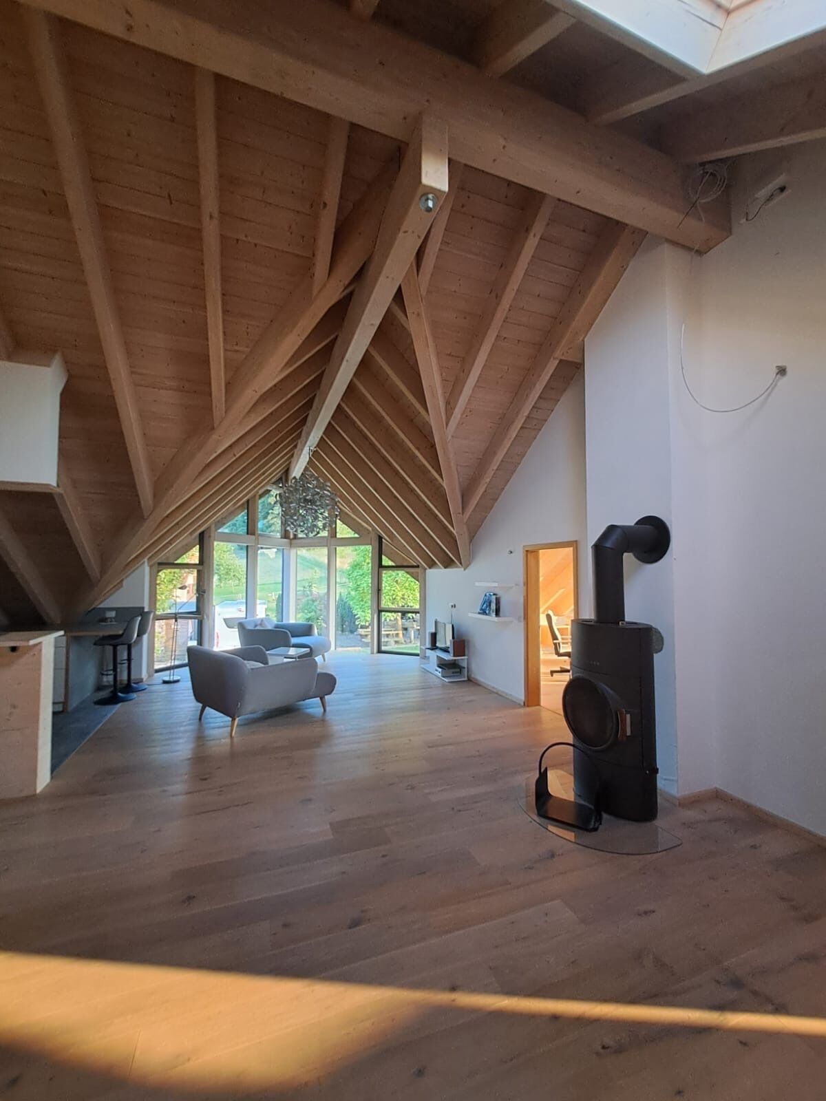 Un loft spacieux avec de hauts plafonds, des poutres apparentes, une cheminée moderne et de grandes fenêtres offrant une vue sur l’extérieur.