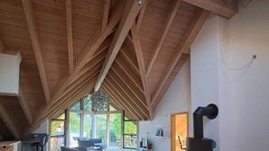 Un loft spacieux avec de hauts plafonds, des poutres apparentes, une cheminée moderne et de grandes fenêtres offrant une vue sur l’extérieur.