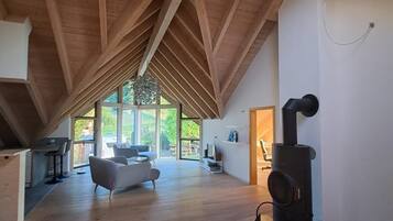 Ein geräumiger Lofts mit hohen Decken, Holzbalken, einem modernen Kamin und großen Fenstern mit Blick ins Freie.