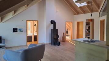 A spacious loft with a high ceiling, wooden beams, a built-in wood stove, and a cozy seating area.