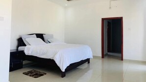 Un dormitorio con cama, mesitas de noche, una puerta y piso de baldosas.