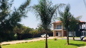 Un barrio residencial con un césped cuidado, varios árboles y una casa de dos pisos con balcón.