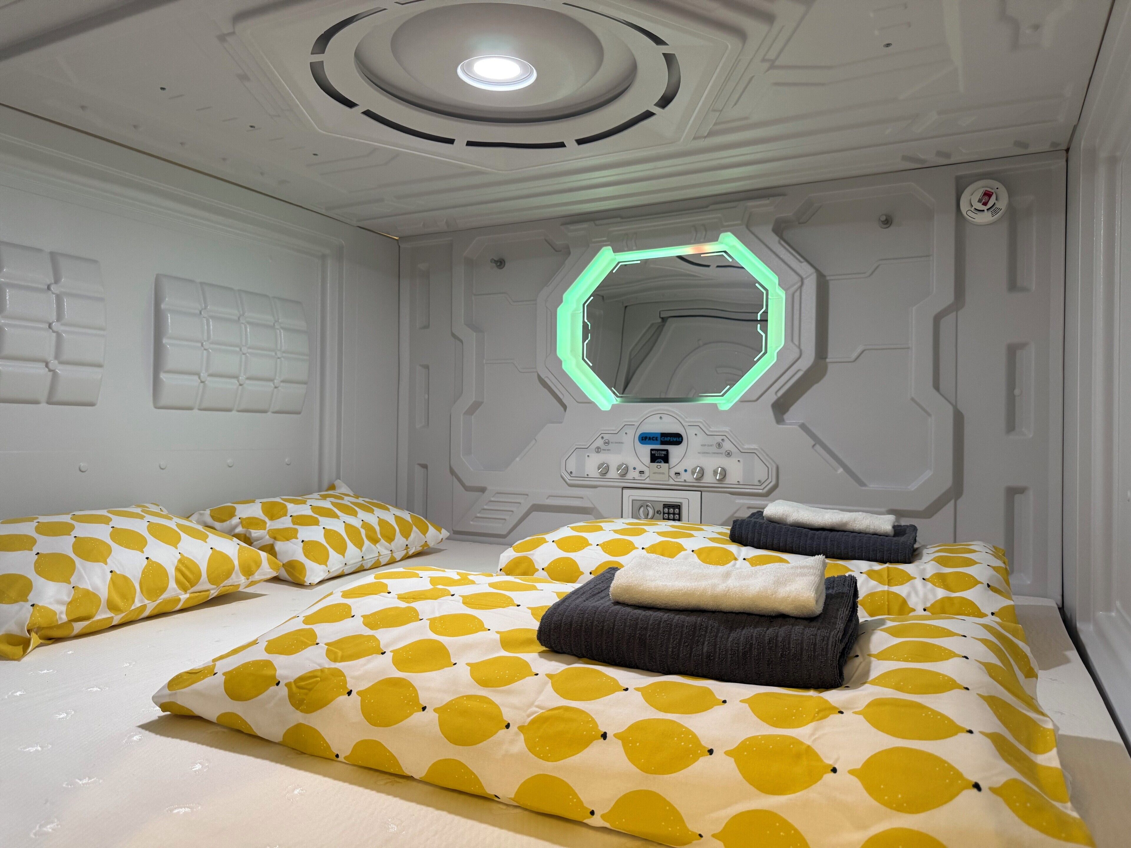 Una habitación con diseño futurista, que presenta un panel de control central, un espejo hexagonal y camas con ropa de cama estampada.