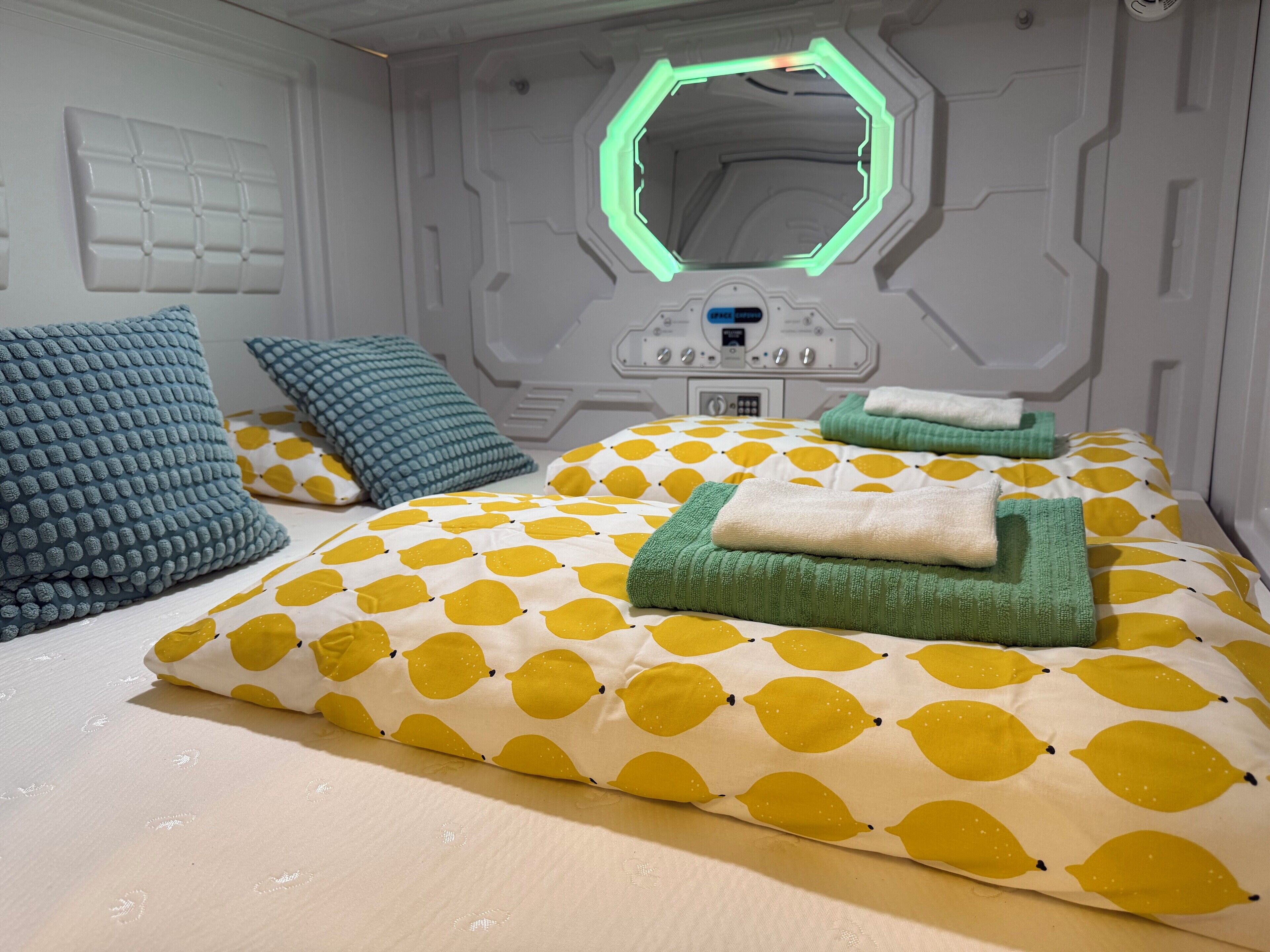 A modern bedroom with a geometric wall design, a bed with yellow and white patterned bedding, and a green neon light on the wall.