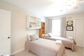 A bedroom with two beds, a wardrobe, a shelf unit, and a window with curtains. - Quail Cove 1617 at Rumbling Bald (Lake Lure)
