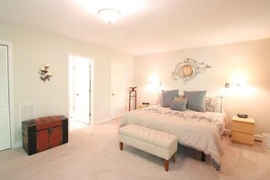 A bedroom with a bed, bedside tables, a bench, a wall clock, and a trunk.