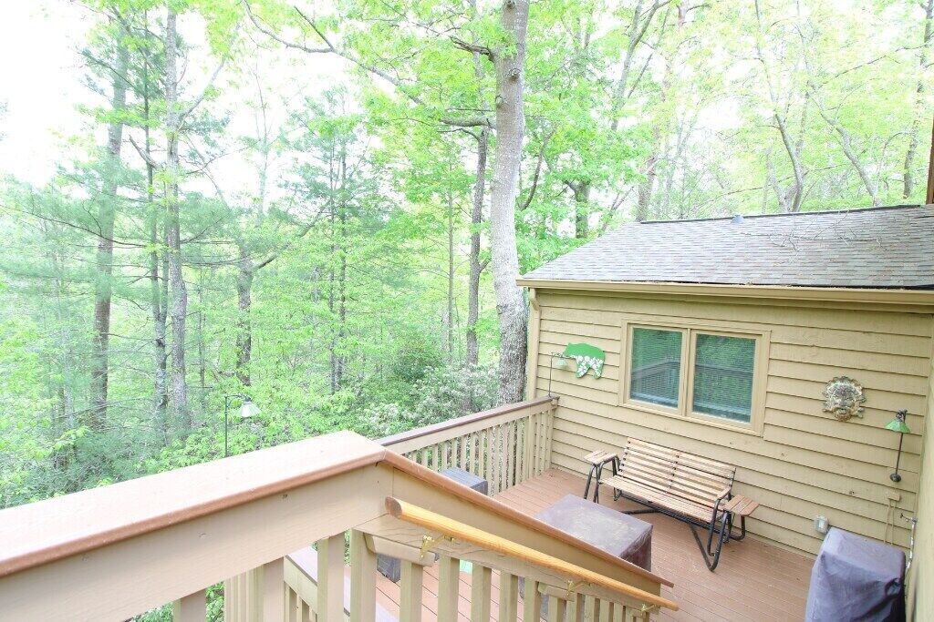 A wooden deck with a bench and table, surrounded by trees.