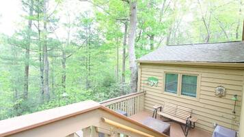 A wooden deck with a bench and table, surrounded by trees.