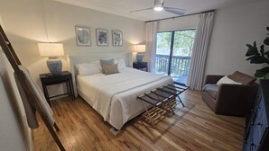 Une chambre à coucher comprenant un lit, des tables de chevet, un ventilateur de plafond, une fenêtre avec des rideaux et une vue sur l’extérieur.
