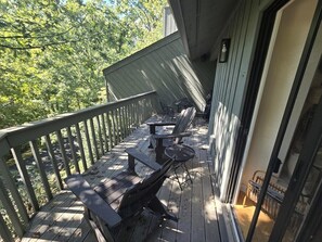 Une terrasse en bois, dotée de mobilier d’extérieur, d’une rambarde et d’une porte donnant sur un espace intérieur.