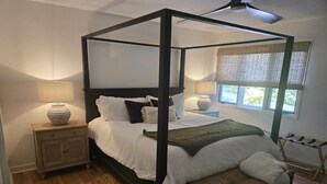 Un lit à baldaquin à quatre poteaux, avec un banc en bois, une table de chevet avec une lampe et une fenêtre avec des stores.