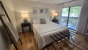 Ein Schlafzimmer mit einem Bett, Nachttischen, einer Lampe, einem Wäscheständer und Blick ins Freie.