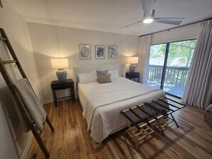 A bedroom with a bed, nightstands, a lamp, a drying rack, and a view of the outdoors. - Quail Cove 1631 at Rumbling Bald (Lake Lure)