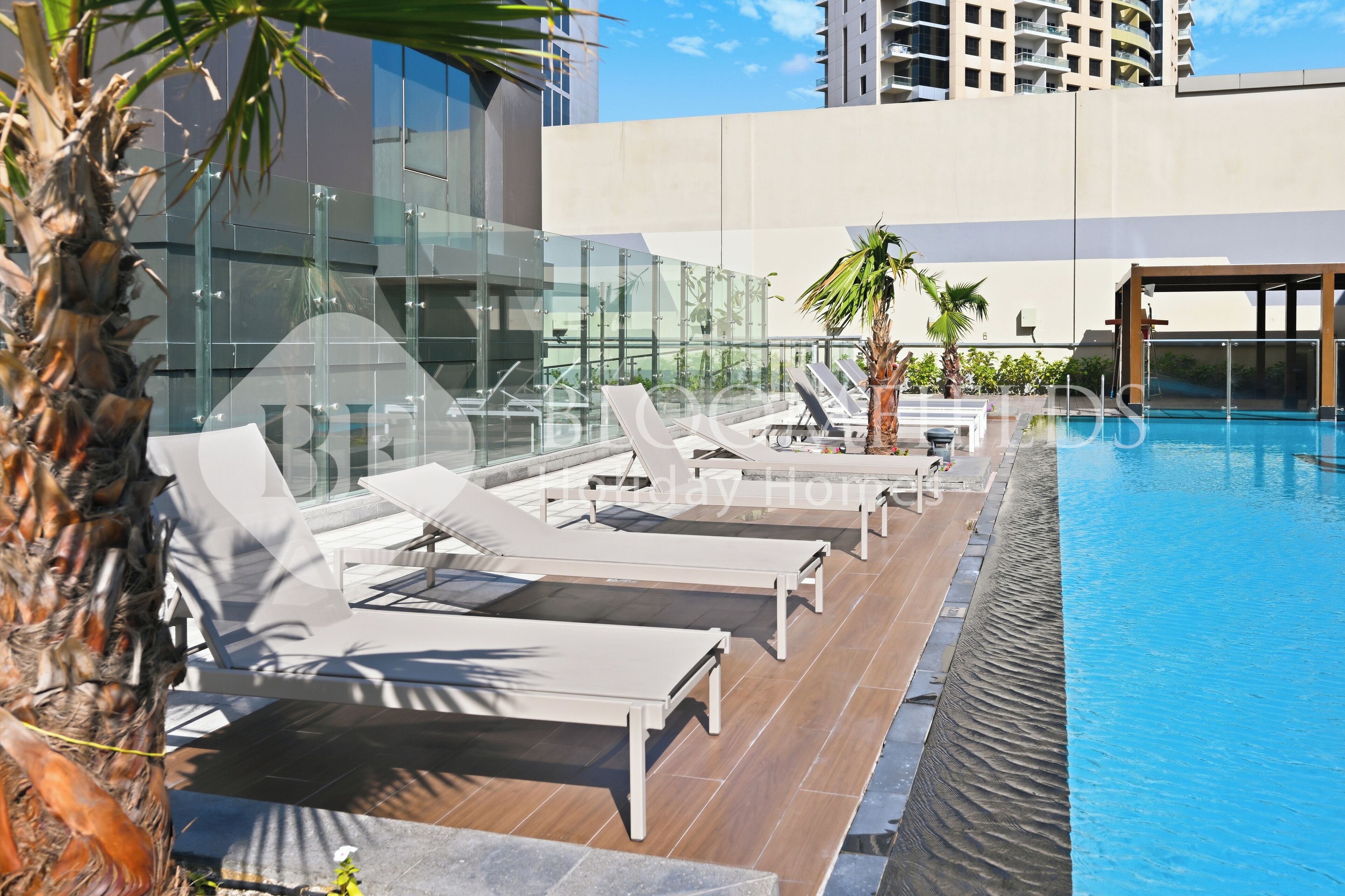 Un espace piscine aménagé sur le toit, avec des chaises longues et des palmiers.