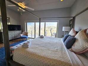 Ein Schlafzimmer mit einem großen Bett, einem Fernseher, einem Sessel und Blick ins Freie.