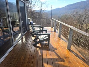 Eine Holzterrasse mit Sitzgelegenheiten und einer Glaswand mit Blick auf eine Berglandschaft.
