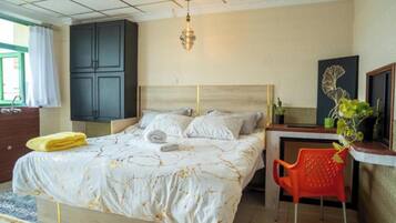A bedroom with a bed, a desk, a chair, a wardrobe, and a hanging light fixture.