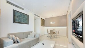 Una sala de estar moderna con sofá, mesa de centro y televisor. Hay un comedor con sillas y una mesa.