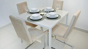 Una mesa de comedor dispuesta con platos, tazones y vasos blancos, rodeada de sillas color beige.