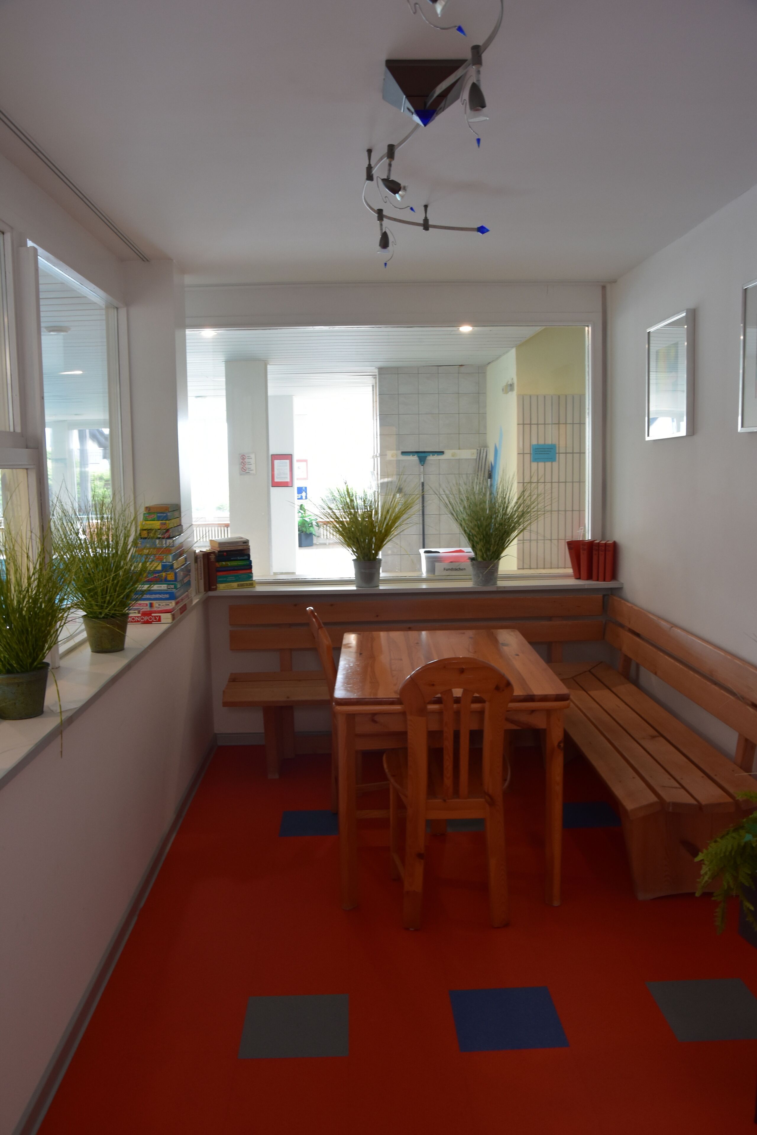 A room with a wooden table and benches, potted plants, and a red carpet.