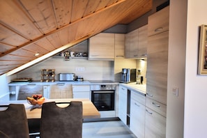 A modern kitchen with wooden beams, built-in appliances, and a dining area with a bowl of fruit.