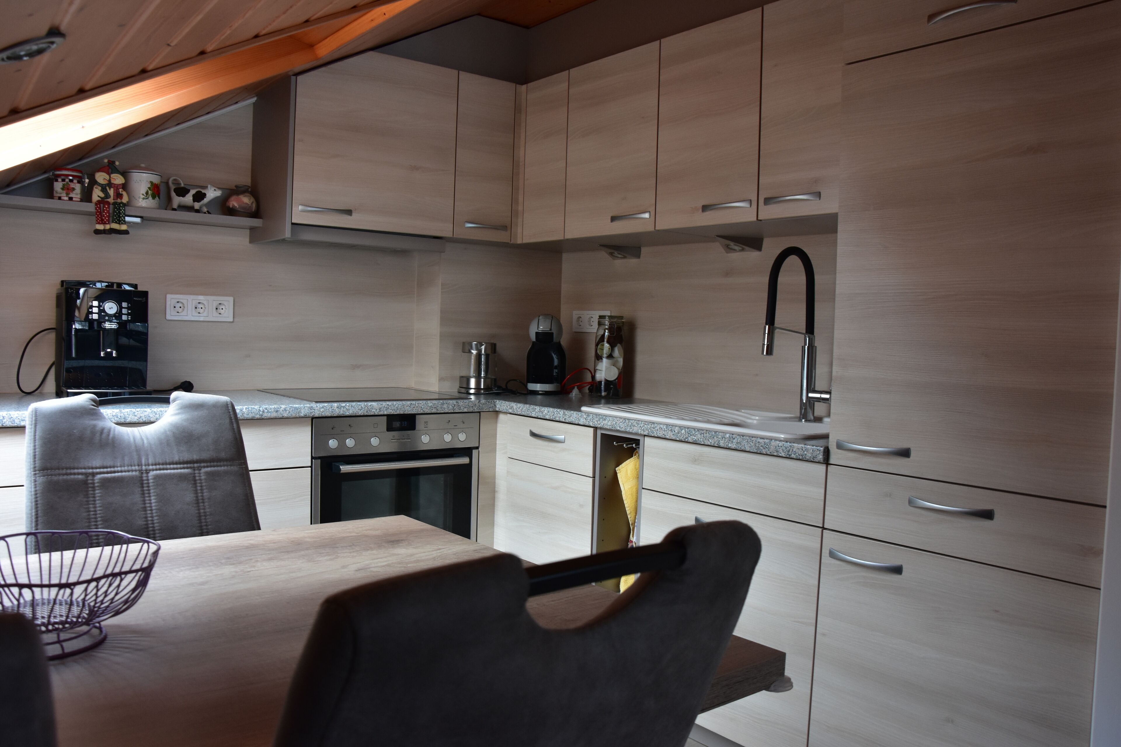 A modern kitchen with light wood cabinets, a stainless steel sink, and a dining area with a table and chairs.