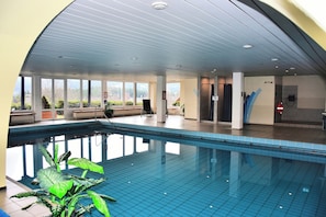 An indoor swimming pool with clear views of the outdoors, a tiled floor, and a ceiling with recessed lighting.
