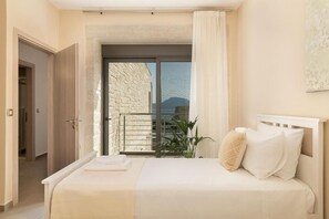 A bedroom with a bed, a view through a window, and a door leading to another room. - Elios Villas (Marathi)
