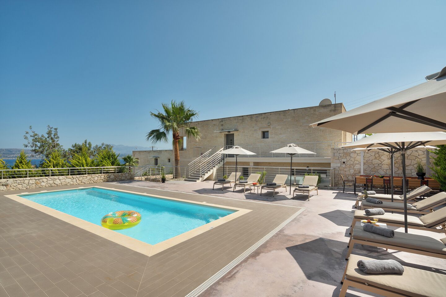 A rooftop pool area with lounge chairs and umbrellas, a stone building, and a view of the sea.