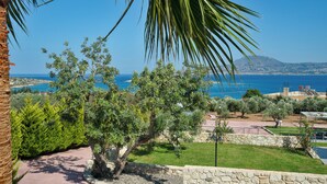 A coastal landscape with a stone wall, a palm tree, and a view of the sea. - Elios Villas (Marathi)