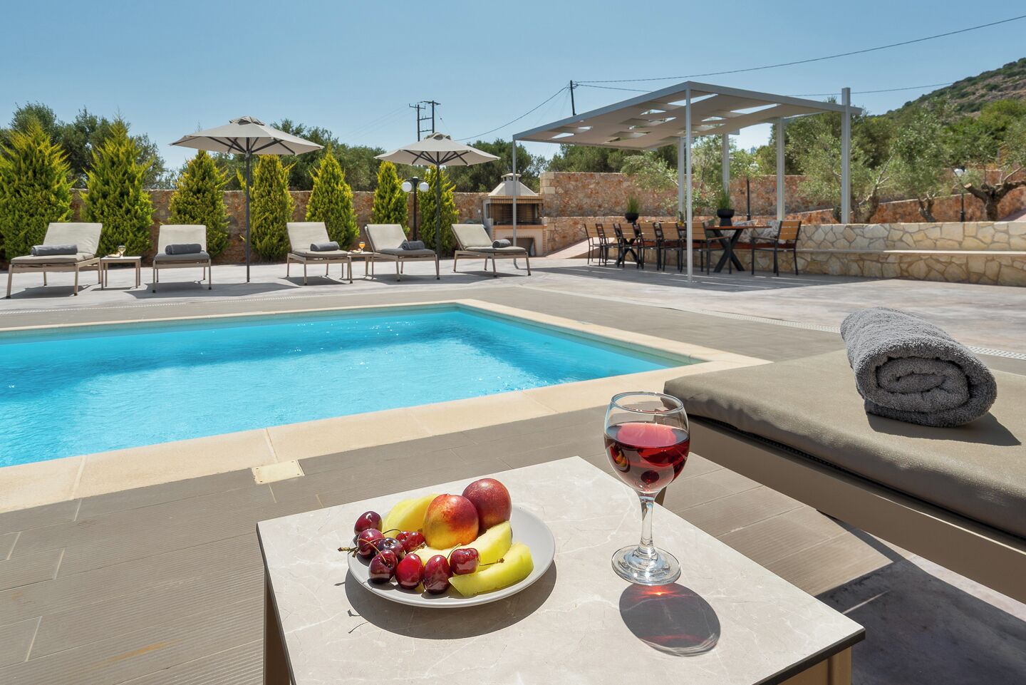 Ein Poolbereich mit Liegestühlen, einem Tisch mit Früchten und Wein sowie einer Pergola.