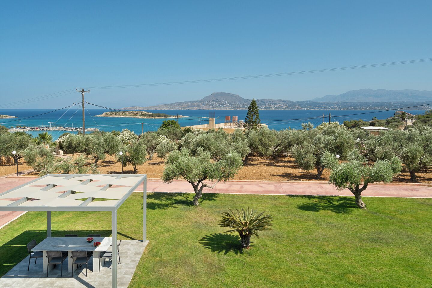 Une terrasse avec une table et des chaises, des oliviers et une vue sur la mer et les montagnes.