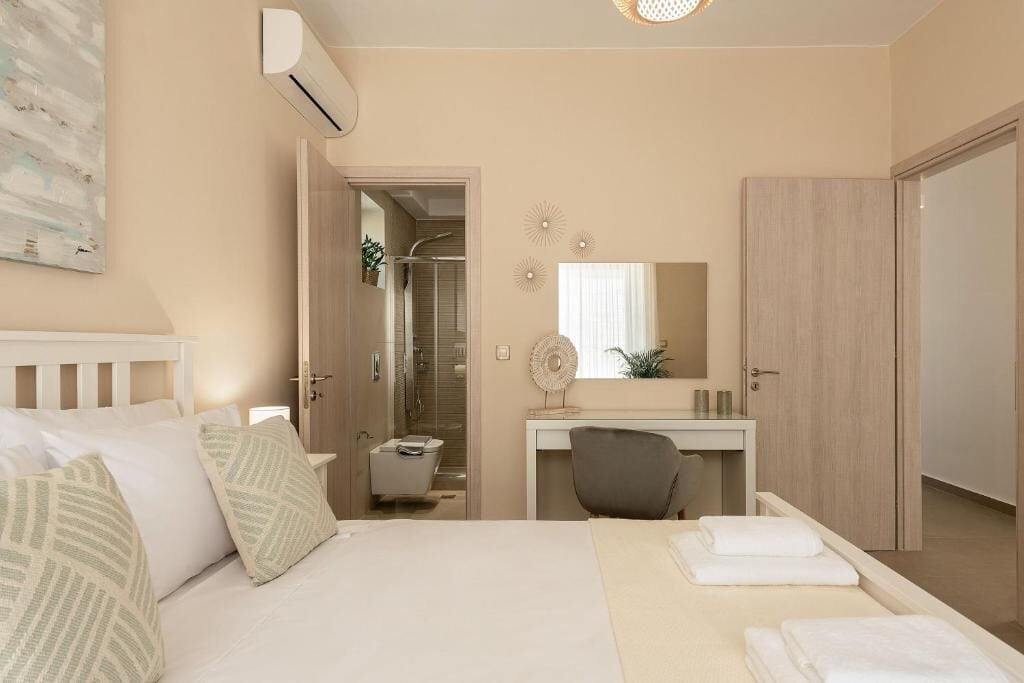 A hotel room with a bed, a desk, a chair, a bathroom, and a door.