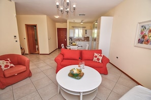 A living room with a red sofa set, a white coffee table, and a kitchen in the background. - Echo One Bedroom Apartment (Pelekas)