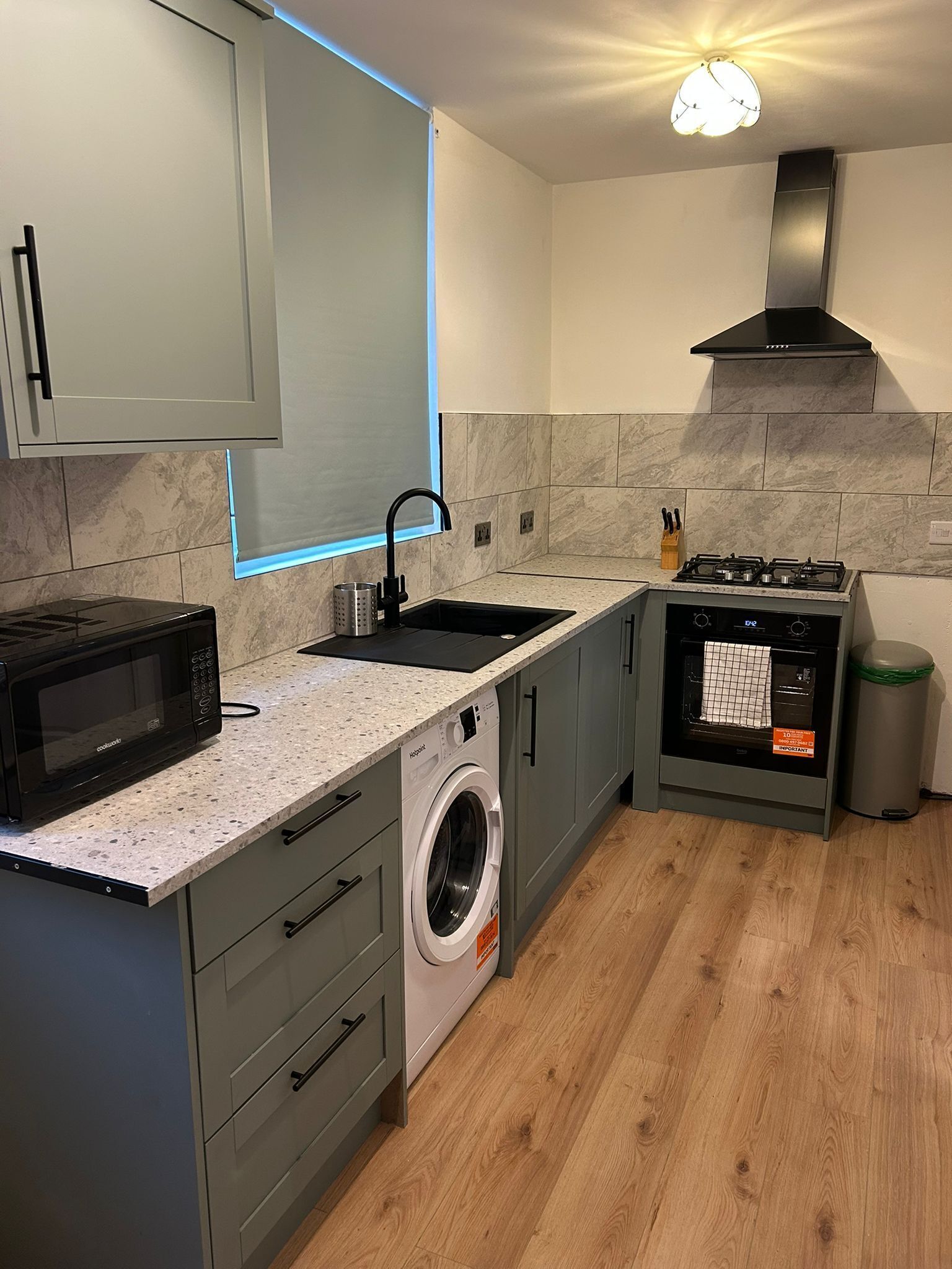 Cocina compacta con microondas, lavadora, fregadero, estufa y un cubo de basura.